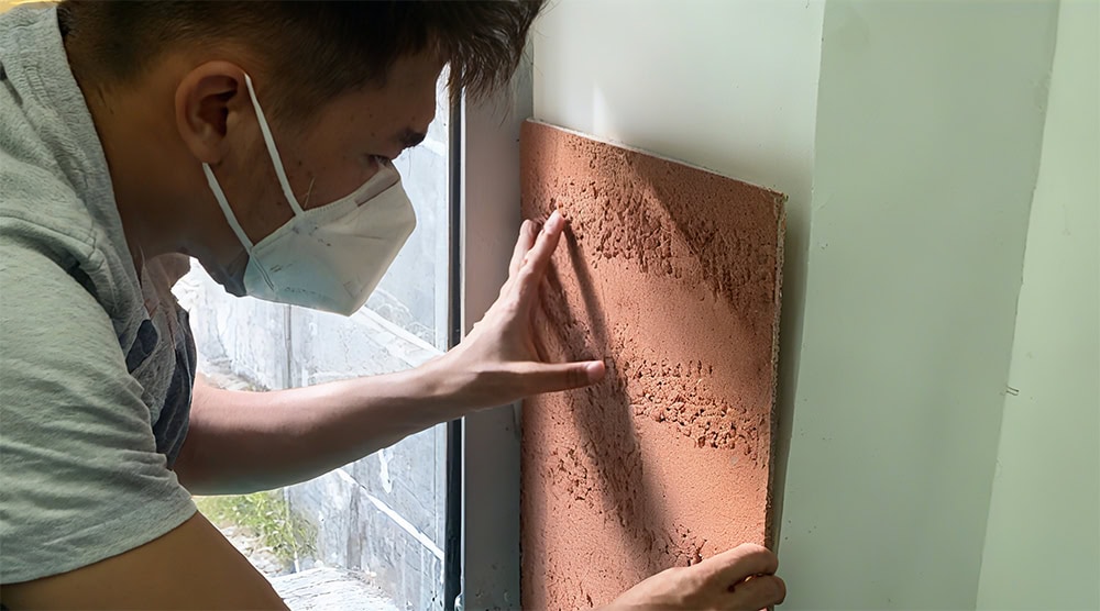 Person placing flexible stone tile on wall near window